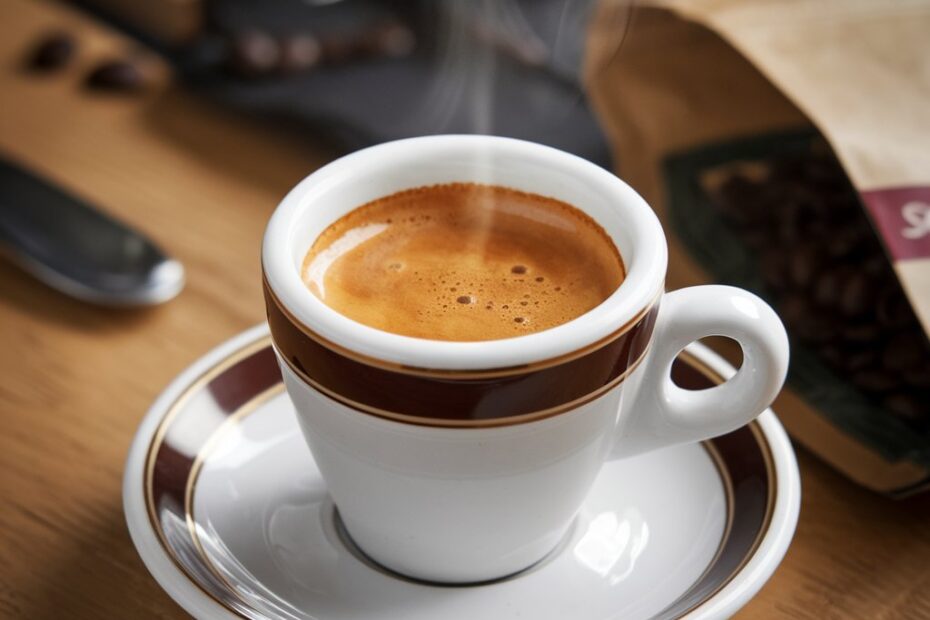 A steaming cup of Arabica coffee surrounded by coffee beans on a wooden table.